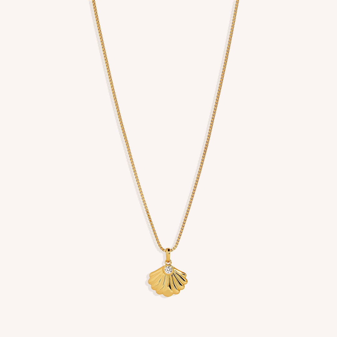 An 18K gold vermeil pendant necklace with an oyster-shaped charm and a white zirconia stone on a gold chain.
