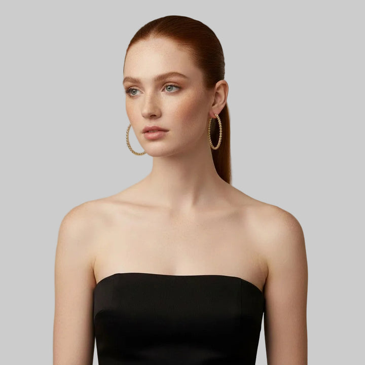 Woman wearing 14K Gold Filled Gilda hoop earrings and a black strapless dress against a neutral background