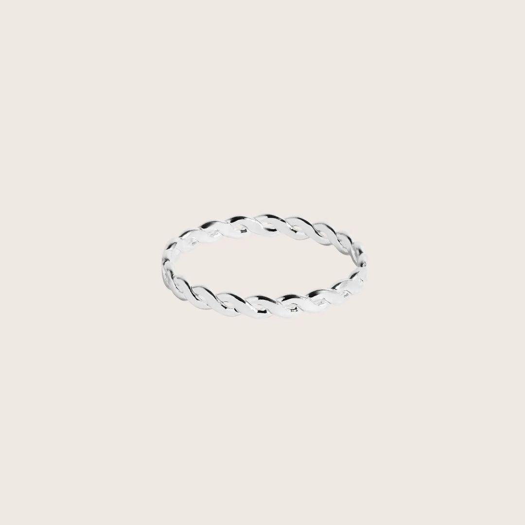 Silver ring with a twisted design on a light beige background