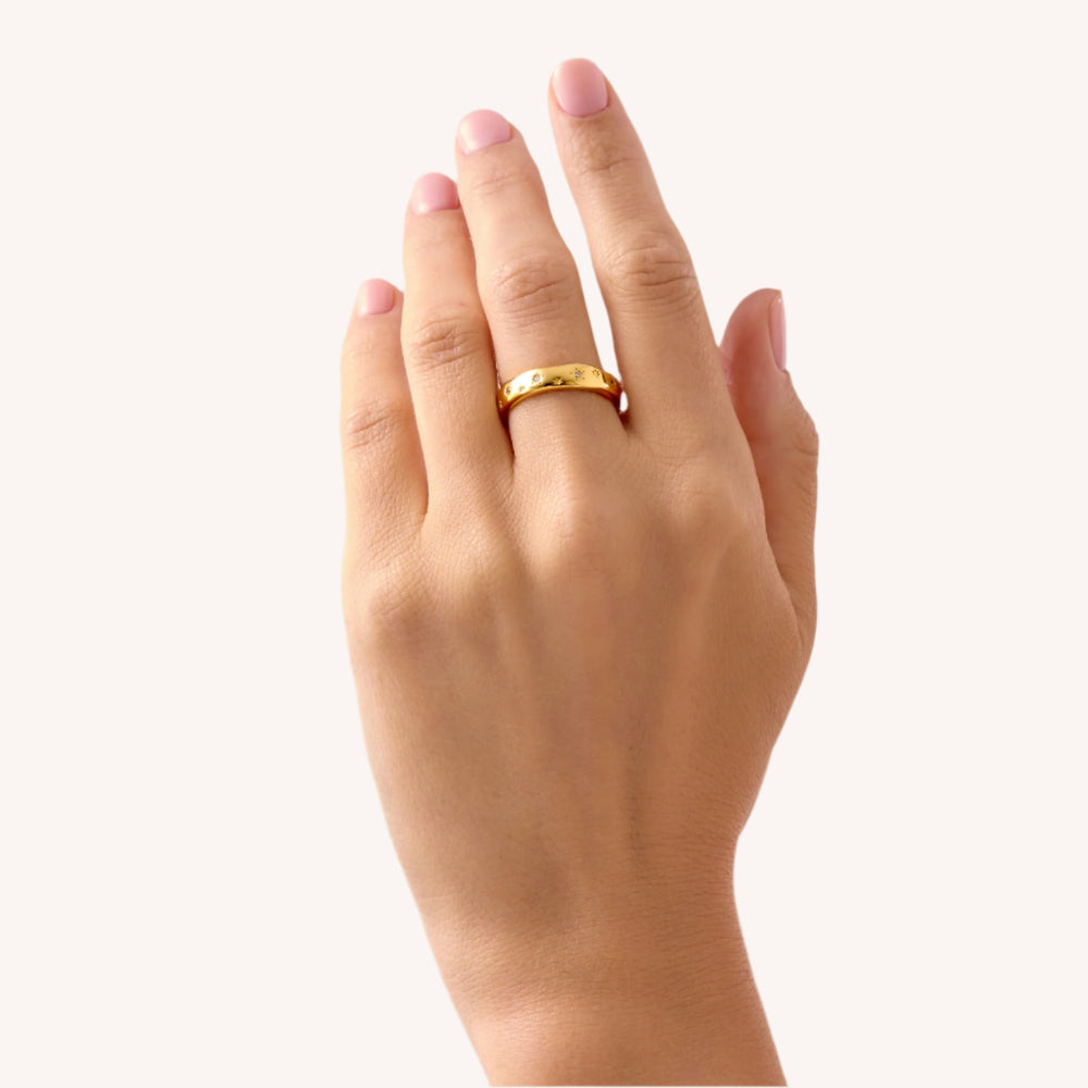 A person's hand displaying a gold-plated ring with bezelled white zircon stones on the finger.