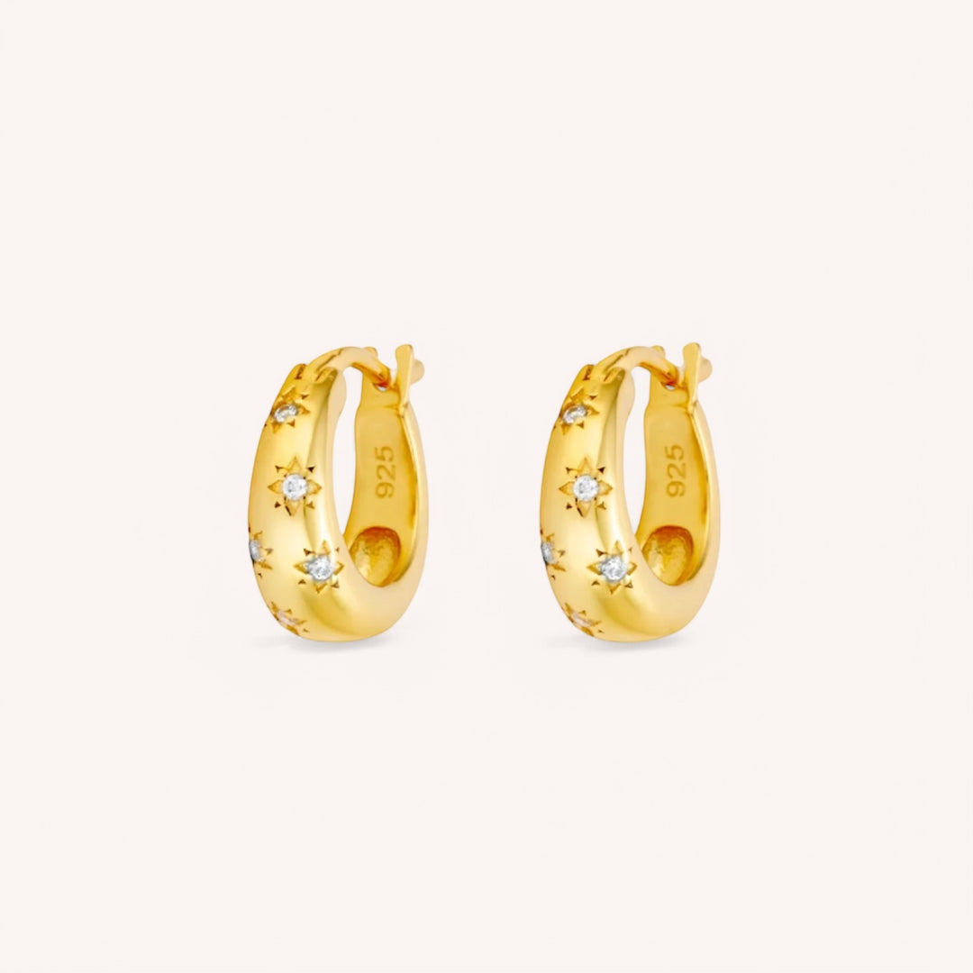 A pair of 18K gold huggie hoop earrings adorned with mini zircon stars.